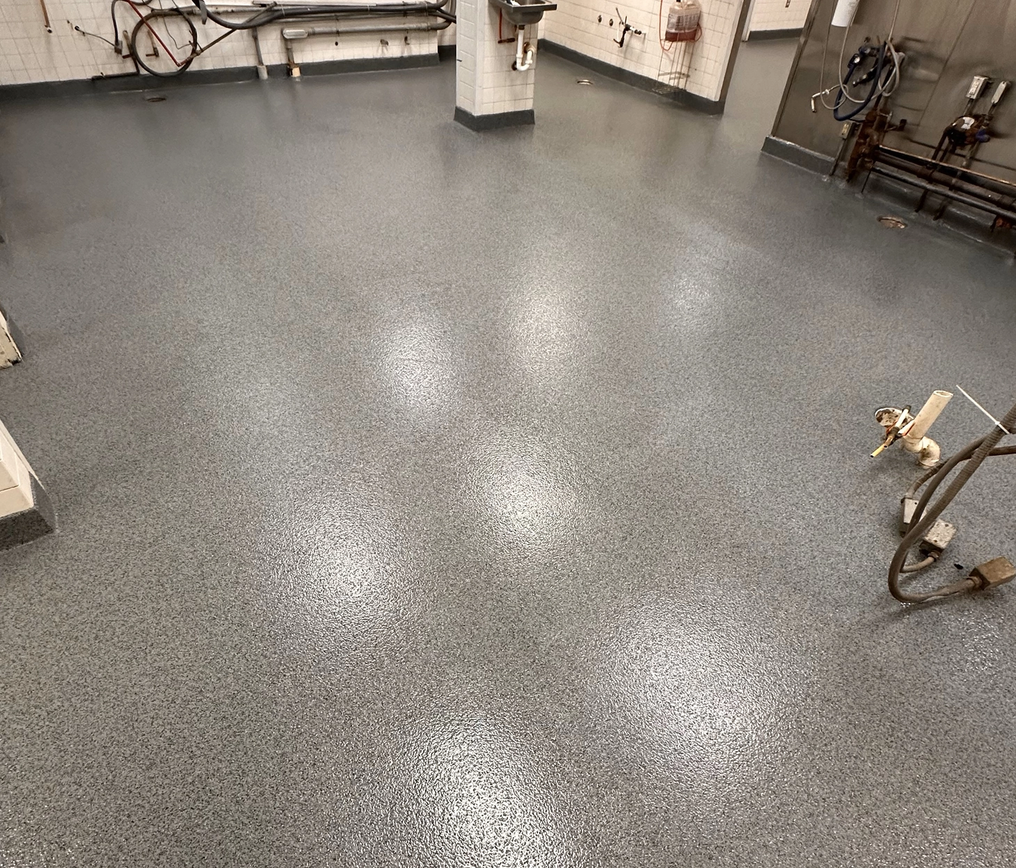 Durable gray epoxy flake flooring in a food-safe industrial environment with visible piping and sinks.