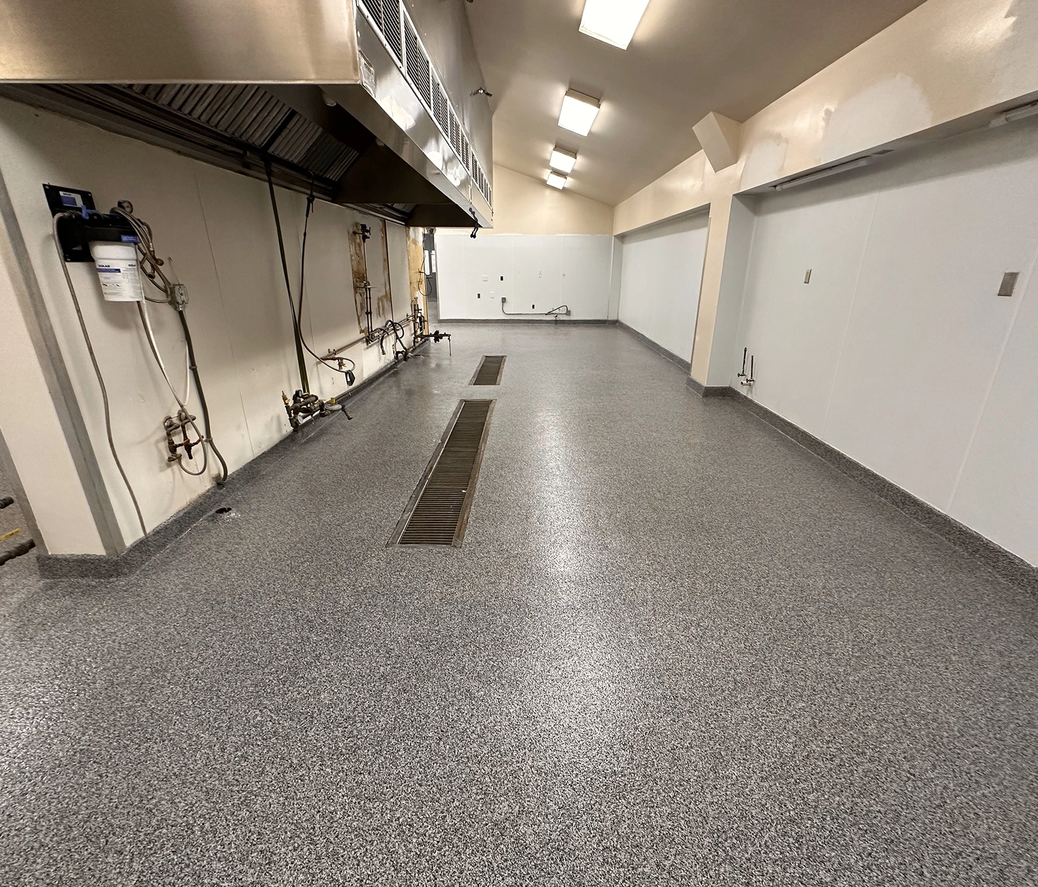 Seamless gray epoxy flake flooring with integrated trench drains in a commercial kitchen or food prep facility.
