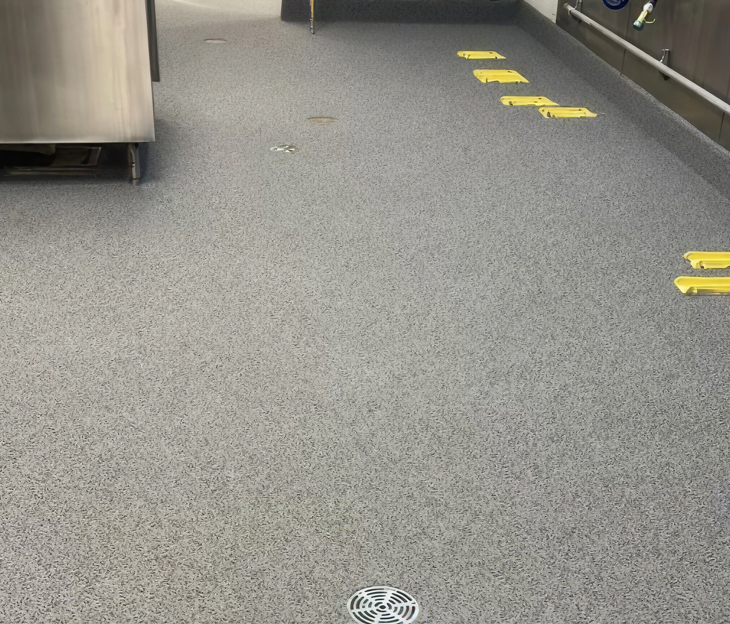 Urethane cement floor in commercial kitchen with integral cove base, stainless steel equipment, and multiple utility access covers